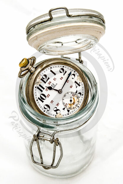 Photo Packshot d'une vielle montre à gousset Omega n'entrant pas dans un bocal de conserve.